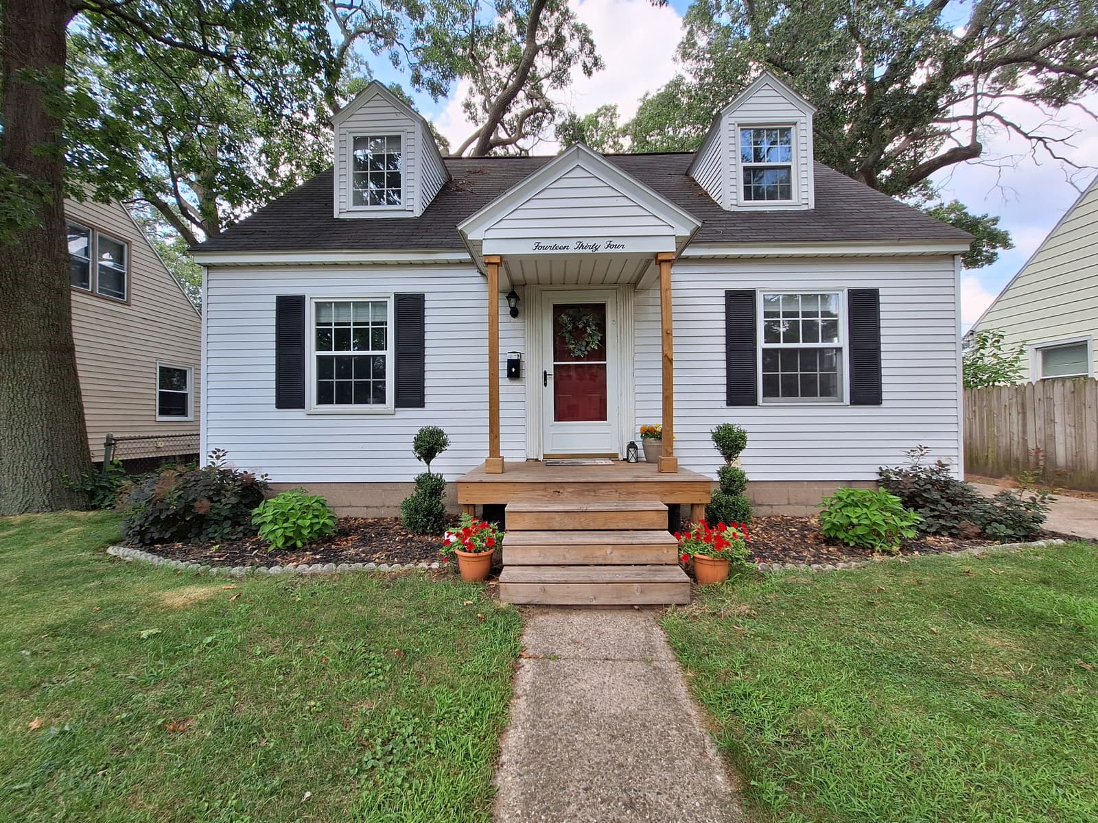 White Cape Cod home with dormer windows, black shutters and a red front door