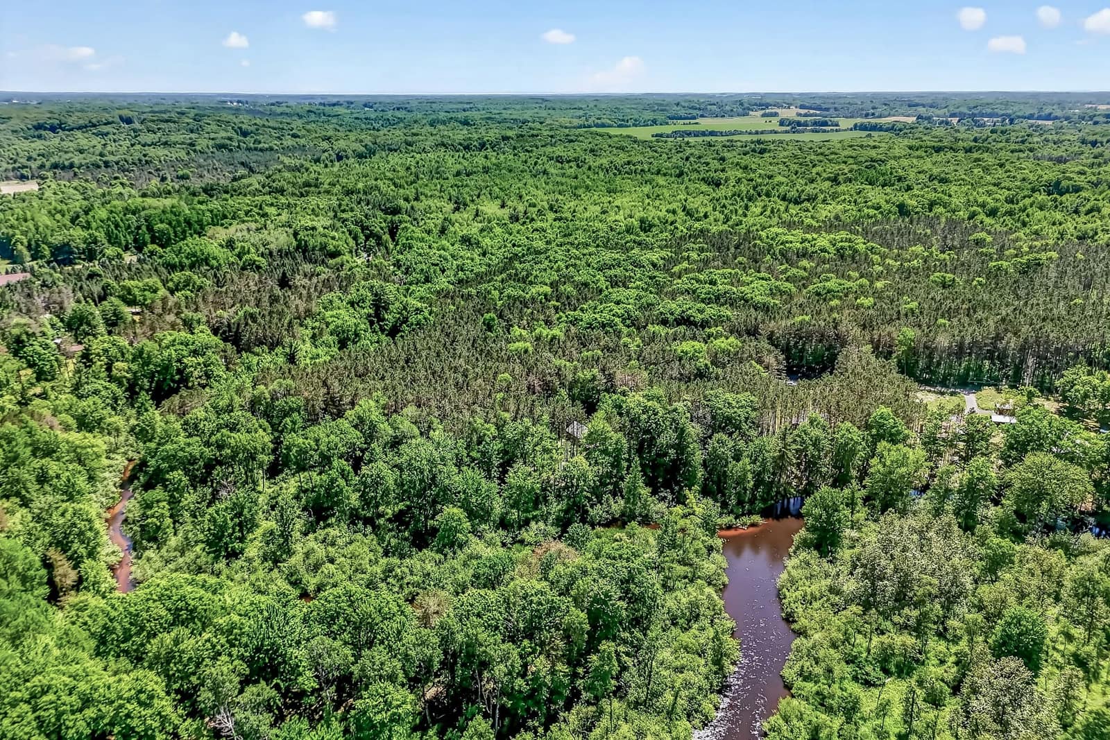 Aerial view of a creek winding through heavy woods on a rural Michigan parcel